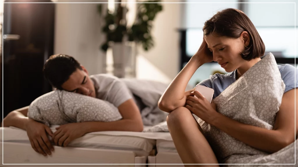 Woman sitting beside bed and man is sleeping on the other side.