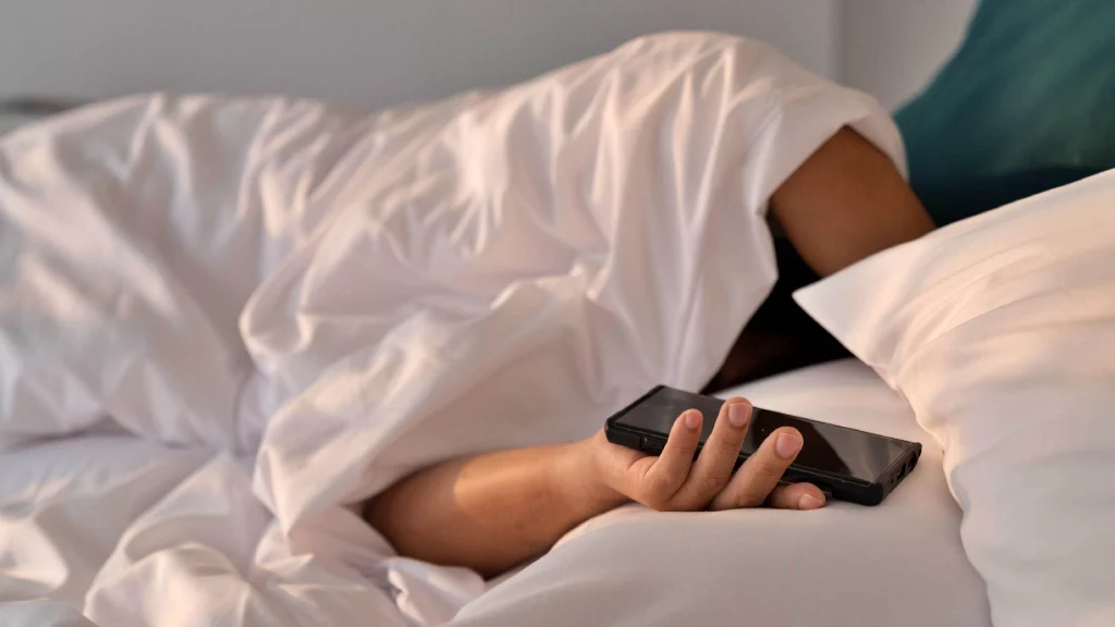 A girl holding her phone on bed while sleeping.