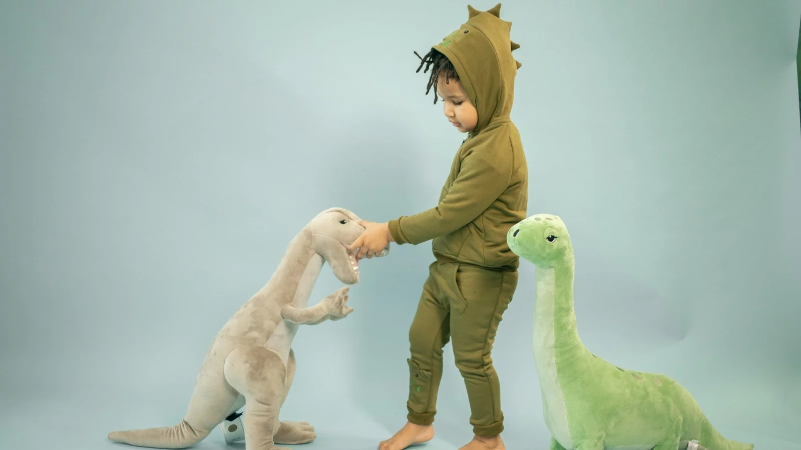 A kid dressed as dinasaur playing with toys.