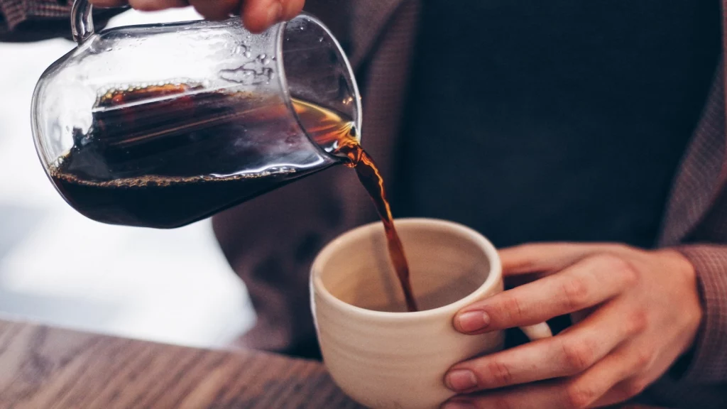 A lady poring black coffee from a jug to her mug