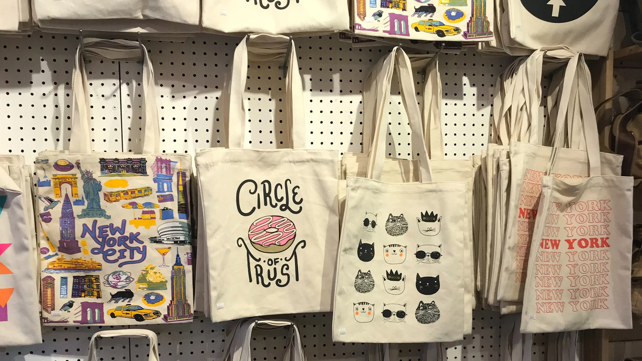 Tote bags of multiple styles hanging in a shop. 