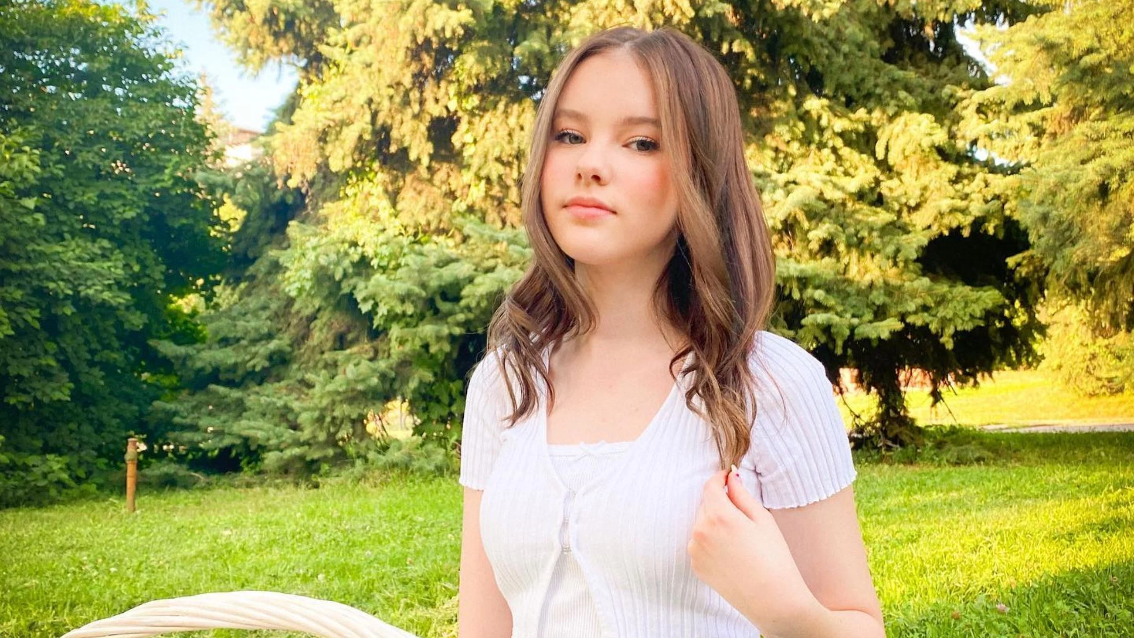 Daneliya sitting in white clothes in a park. 