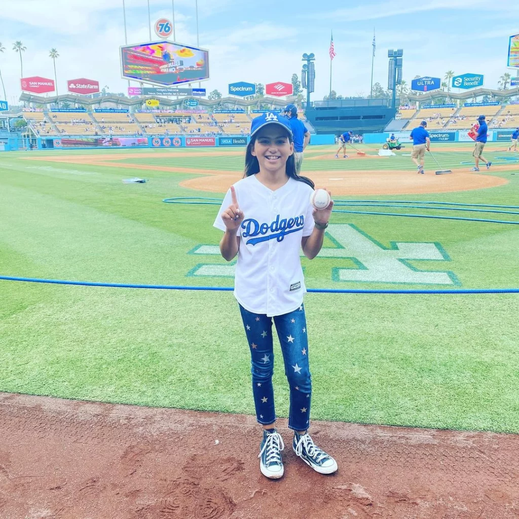 Madison in the sports stadium wearing white jersey and blue jeans and cap.